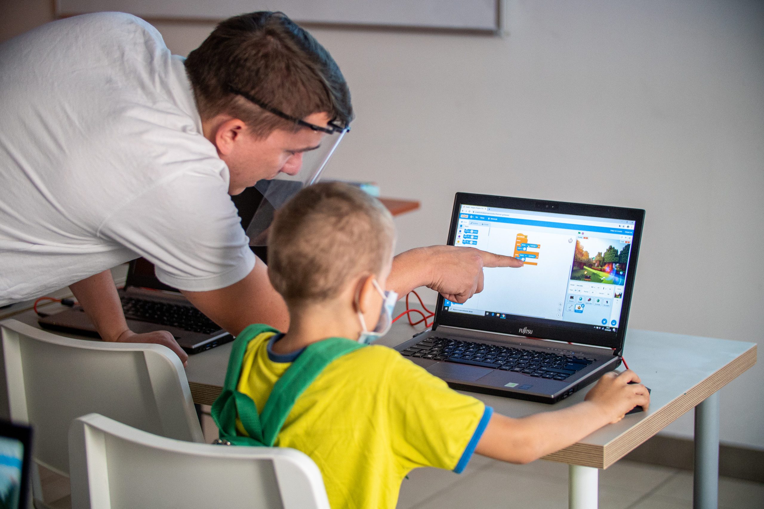 prowadzący pokazuje na ekranie chłopcu jak ma ustawiac kafelki w Scratch