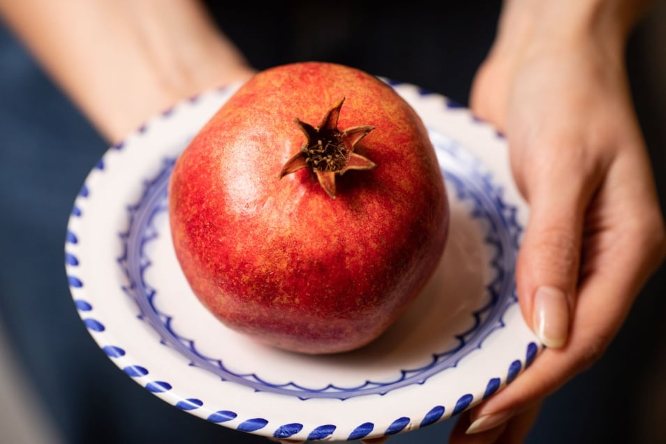 owoc granatu na małym talerzyku trzymanym w kobiecych dłoniach