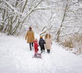 Rodzice z dziećmi idą po śniegu przez las
