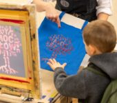 chłopiec dotyka torby wykonanej metodą sitodruku. Nadruk przedstawia drzewko z napisem: Moc słów