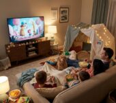 Rodzina siedząca na kanapie w przytulnym salonie, wspólnie oglądająca film z miską popcornu, tworząca domowe kino z ...