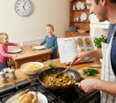 Uśmiechnięta mama przygotowuje szybki, zdrowy obiad dla rodziny w kuchni, trzymając garnek i świeże warzywa, czas pon...
