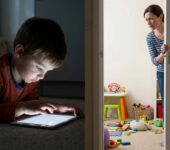 Dziecko wpatrzone w ekran monitora w ciemnym pokoju, ilustrujące problem uzależnienia od gier komputerowych i cyfrowego ...
